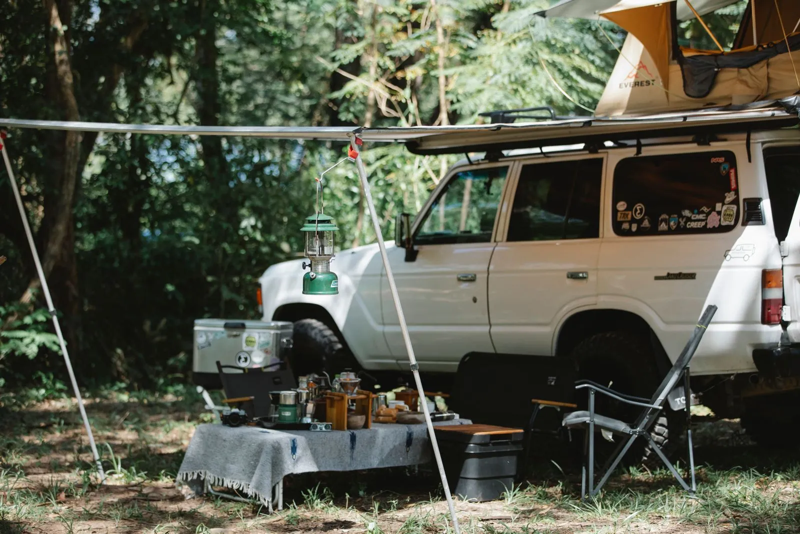 Off-road SUV with rooftop tent and awning parked in a green forest