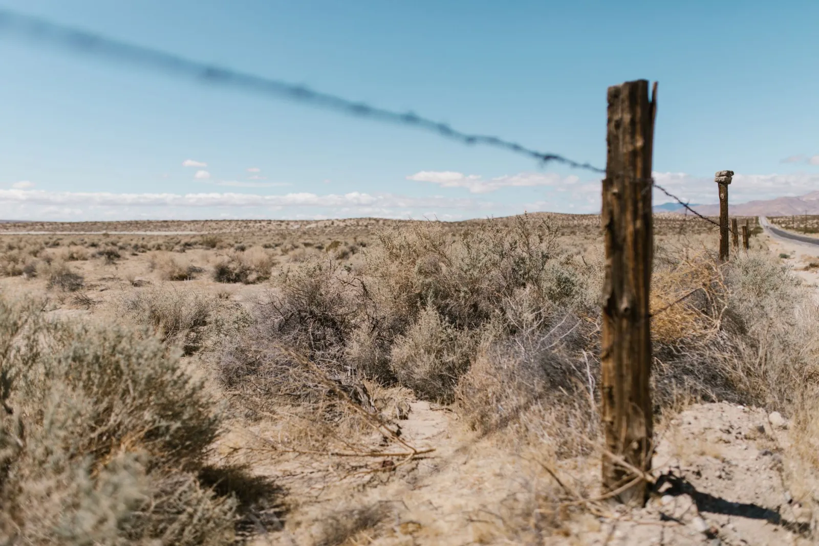 A barbed wire fence line running through sagebrush flats toward distant mountains