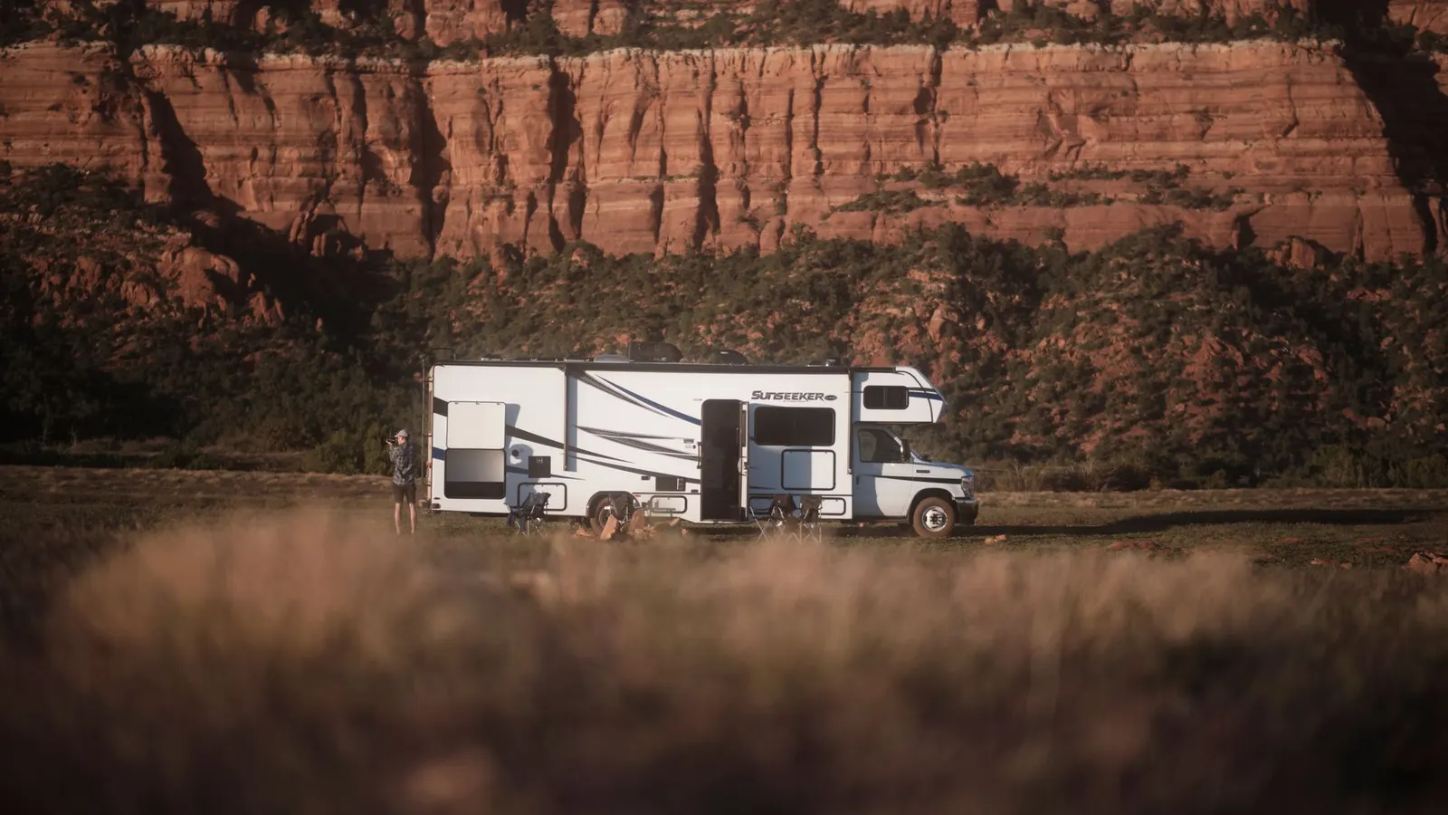 A camper parked below red rock cliffs at a dispersed site
