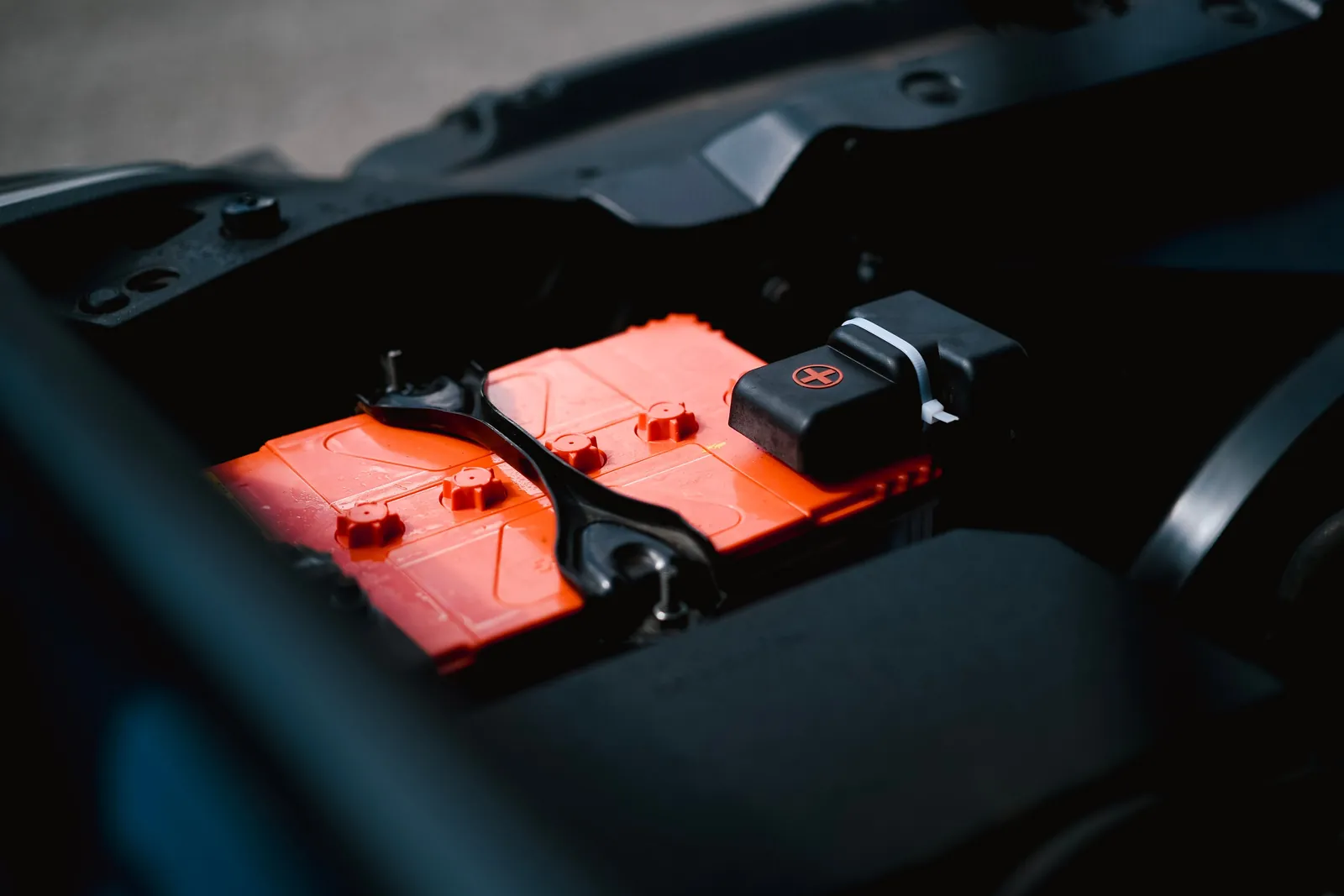 A lead acid battery mounted in a vehicle engine bay with its cell caps and terminal cover visible