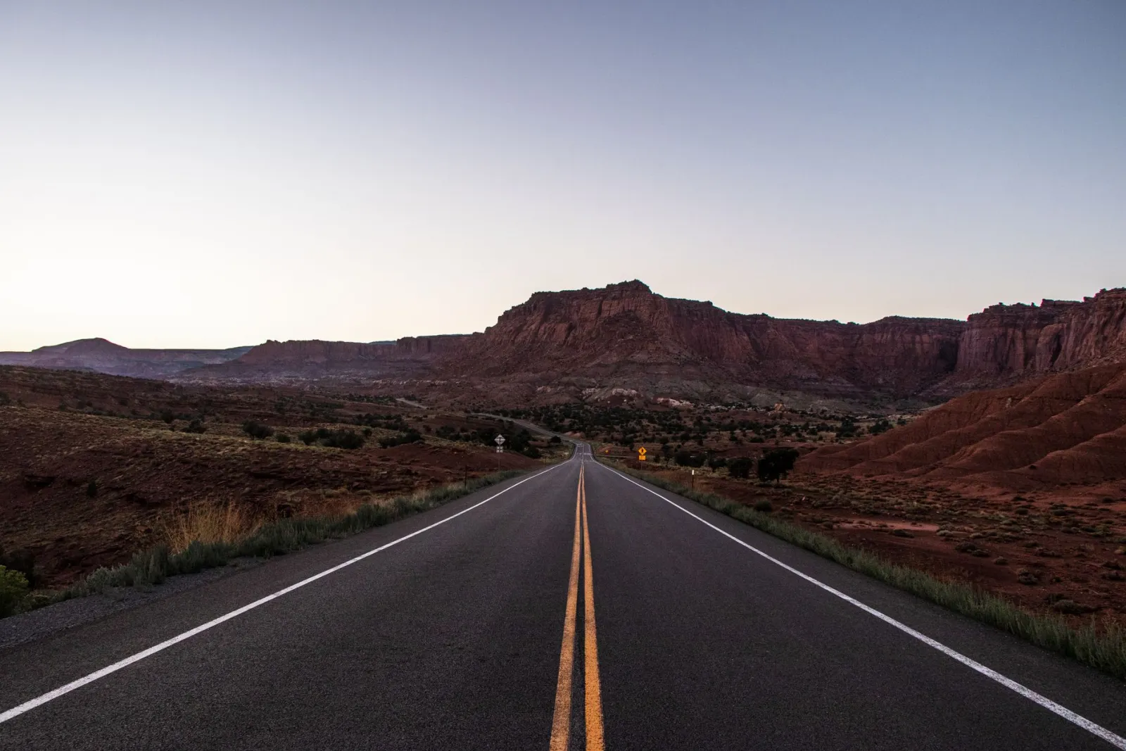 An empty desert highway running toward red rock country in Utah at sunrise